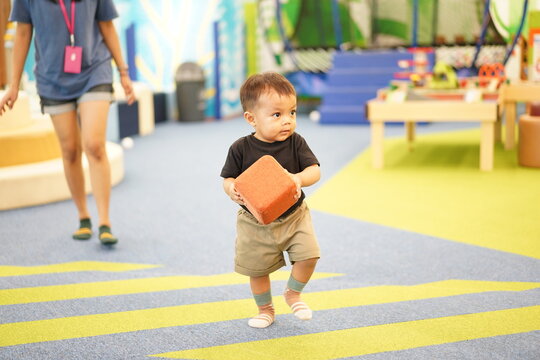 Toddler boy carrying a large foam block while walking in a playground area