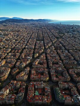 Aerial view of the iconic grid-patterned city blocks of the Eixample district and the Sagrada Familia basilica under a clear blue sky in Barcelona, Catalonia, Spain.