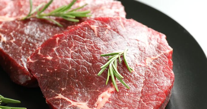 Raw beef steaks and rosemary on table, closeup