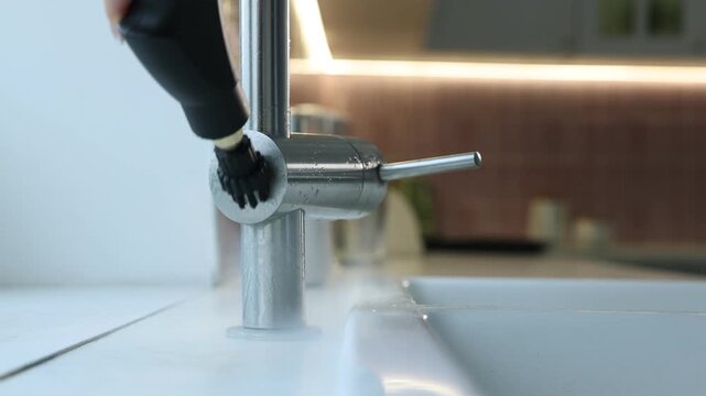 Cleaning faucet with steam cleaner at home, closeup. Camera moving backwards