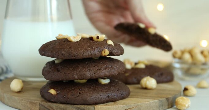 Woman breaking tasty chocolate cookie with hazelnuts at table, closeup