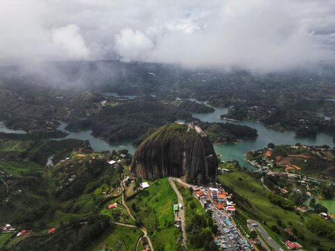 Aerial view of El Penon de Guatape monolithic rock surrounded by the turquoise waters of the reservoir and lush green hills under a cloudy sky in Guatape, Antioquia, Colombia.