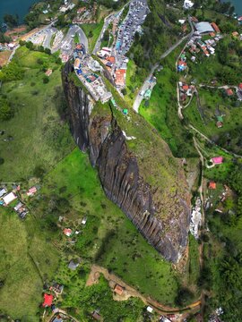 Aerial view of El Penon de Guatape, a massive monolithic rock with a viewing platform on top, surrounded by lush green hills and rural houses in Guatape, Antioquia, Colombia.