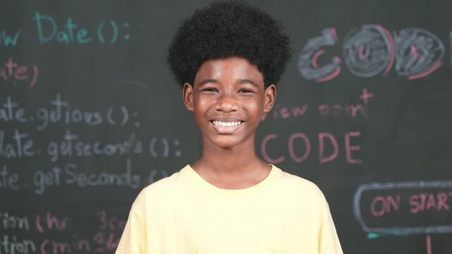 African adult smiling to camera while standing at blackboard with engineering code or prompt. Closeup of handsome teenager wearing casual cloth while attend in STEM technology class. Edification