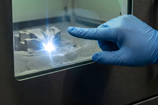 Close up technician monitoring direct metal laser sintering titanium 3D printer in aerospace factory.