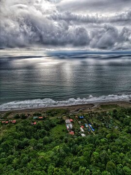 Aerial view of Bahia Solano coastline with lush tropical jungle, sandy beach, and dramatic clouds over the Pacific Ocean in Mutis, Choco, Colombia.
