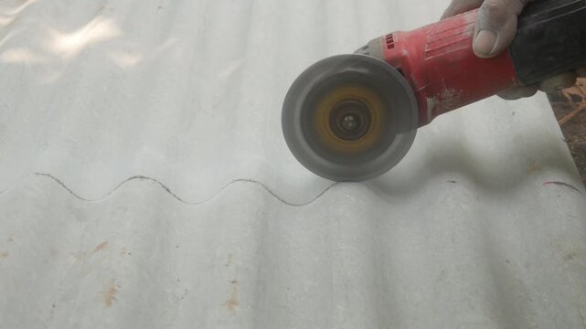 A construction worker uses a hand grinder to cut asbestos or fiber cement roofing sheets.