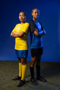 African American female soccer teammates standing back to back on turf wearing jerseys and cleats