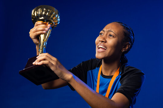 African adult woman athlete holding gold trophy with orange ribbon and sports shirt in studio