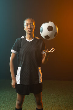 African American female soccer player in kit balancing soccer ball above right hand on studio turf