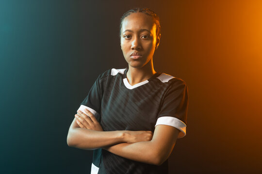 African woman posing arms crossed in black jersey white trim in studio with teal orange lighting