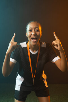 African American female shouting, pointing on turf lit teal amber, wearing whistle and jersey