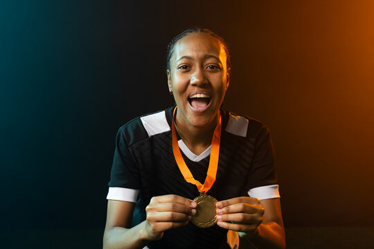 African American woman holding gold medal and cheering in studio with black jersey and braided hair