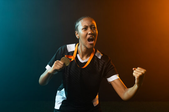 African American woman cheering, holding gold medal orange ribbon, pumping fist in studio in jersey