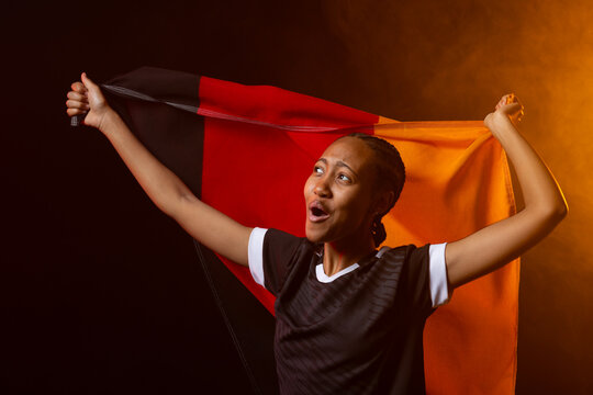 African American woman shouting while holding tricolor flag at studio, wearing sports shirt
