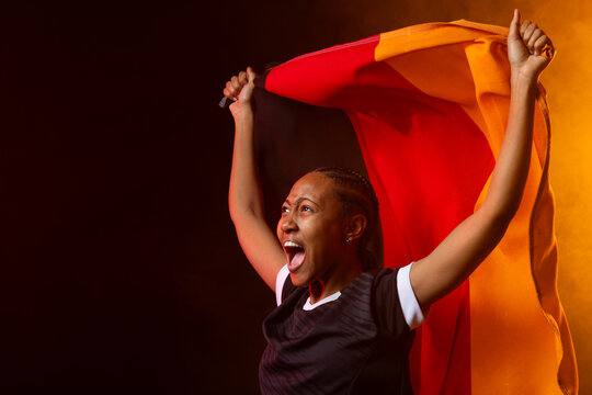 African woman shouting and holding tricolor flag overhead wearing black sports jersey in studio