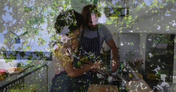 Cooking couple preparing meal in home kitchen, wearing striped aprons with pan, board, leaf overlay
