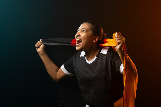 African woman in black jersey cheering while pulling black or red scarf and orange cloth in studio