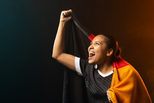 African-American female cheering in black jersey holding flag in studio under gels, copy space