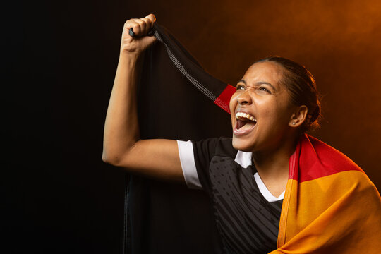 Woman cheering, raising tricolor flag cloth above head in studio, wearing black jersey