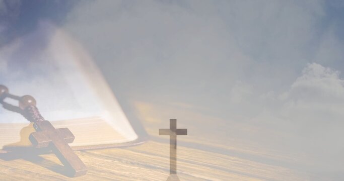 Resting wooden rosary and open book lying on wooden tabletop, with small upright cross silhouette