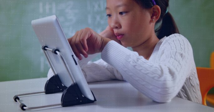 Studying Chinese girl using tablet at school desk, wearing sweater-headband near chalkboard