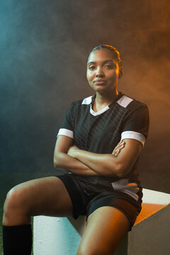 Woman sitting on white cube in studio wearing black jersey, knee-high socks, haze creating gradient