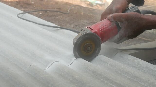 A construction worker uses a hand grinder to cut asbestos or fiber cement roofing sheets.