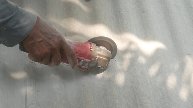 A construction worker uses a hand grinder to cut asbestos or fiber cement roofing sheets.