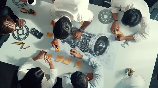 Top view of engineer team writing idea on sticky notes at meeting while discussing about turbine engine or electric generator at meeting table with metal gear, calculator and equipment. Alimentation.
