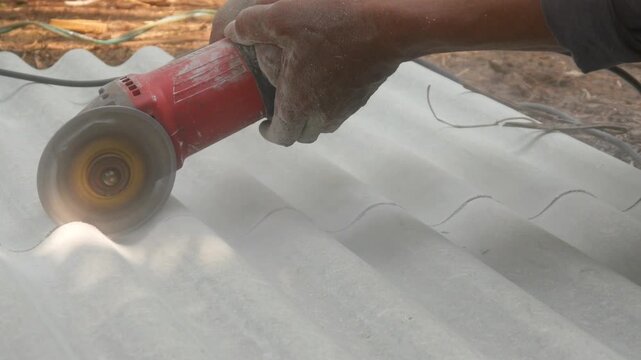 A construction worker uses a hand grinder to cut asbestos or fiber cement roofing sheets.
