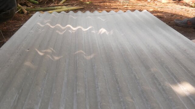 Construction workers are marking cutting lines on corrugated asbestos roofing sheets using a pencil and measuring tool.