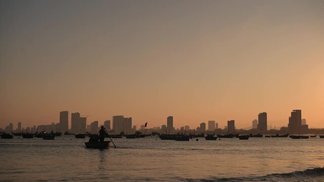 Rowers Navigate Peaceful Waters At Sunrise. Quiet Dawn As Asian Coracle Paddlers Drift Smoothly Along. Calm Early Morning Scene With Round Boats And Silhouetted Skyline In Vietnam