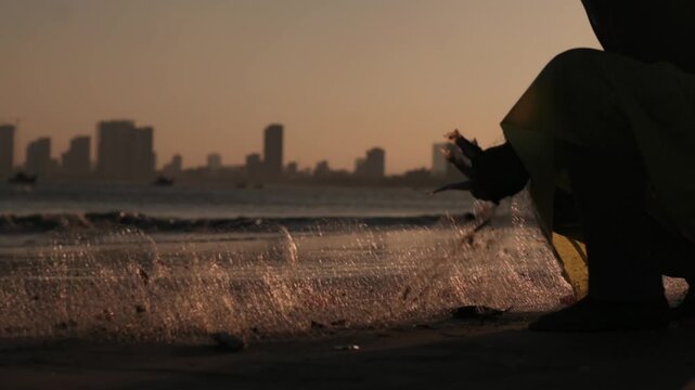Asian Fisherwoman Repairing Fishing Net On Da Nang Shoreline Sunrise Hands Pulling Wet Mesh Droplets Sparkling In Golden Backlight City Skyline Distance Focused Tactile Labor