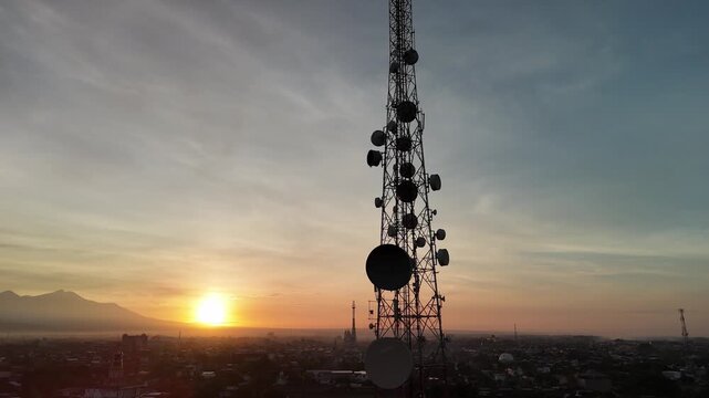Telecommunication tower silhouette with microwave dish antennas against a golden sunrise city skyline
