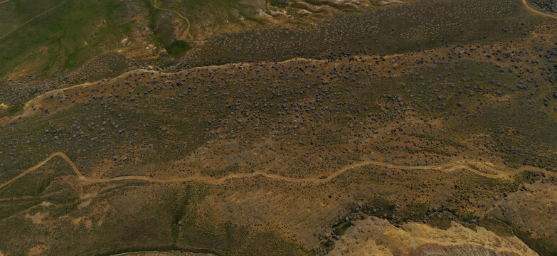 Aerial view of the Valley of Balls featuring unique spherical rock formations and a winding dirt road across the arid desert landscape in Mangistau, Mangystau Region, Kazakhstan.