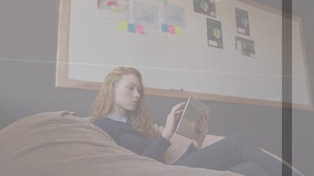 Woman student reclining on beanbag tapping tablet, initiating animated design notes on whiteboard