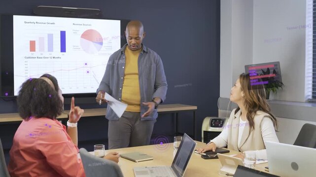 Standing presenter pointing to charts and placing handouts, guiding colleagues through sales data