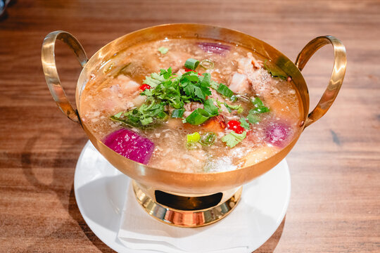 Thai spicy spare rib cartilage soup served in a copper pot, garnished with chopped cilantro and scallions.