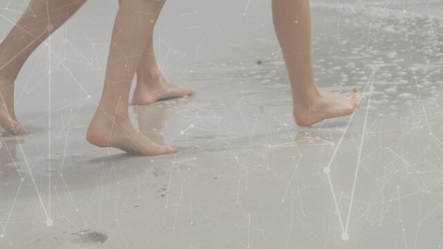 Two barefoot walkers walking shore, surf reaching feet and erasing footprints for leisure
