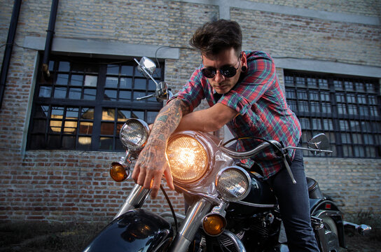 Handsome guy with sunglasses on vintage motorcycle posing outdoors by the old factory 
