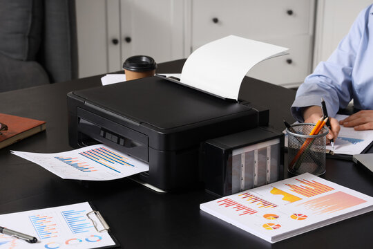 Businesswoman with modern printer and diagrams working on table in office