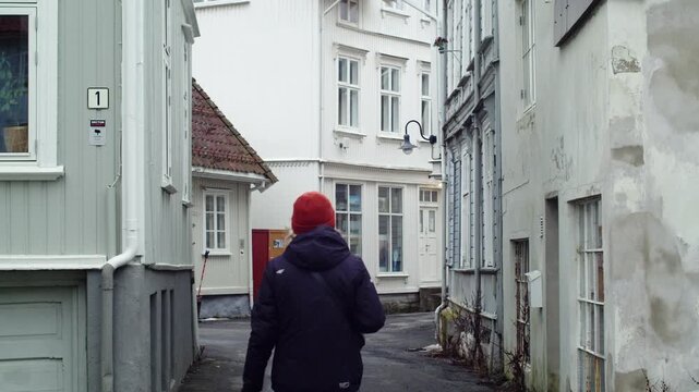 A young woman in winter clothing walking through the narrow streets of Krager&oslash;, Telemark, Norway, surrounded by white wooden architecture