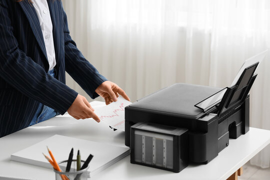 Businesswoman using printer on desk in office