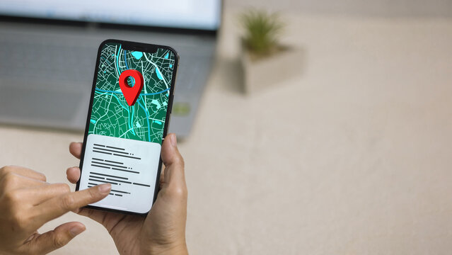 Hand holding smartphone showing digital city map with red location pin on screen.