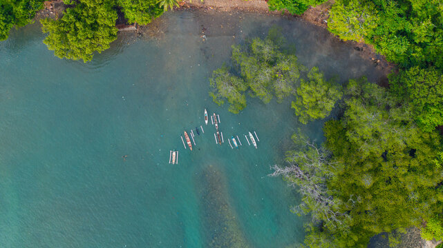 Aerial view of traditional outrigger boats anchored in turquoise water near the lush tropical shoreline of We Island, Sabang City, Aceh, Indonesia.