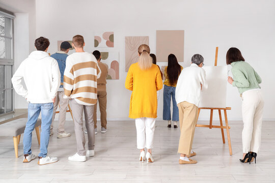 Group of people looking at paintings in art gallery, back view