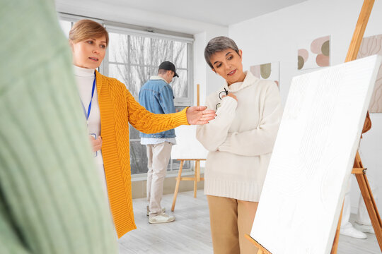 Female guide showing painting to people at exhibition in art gallery