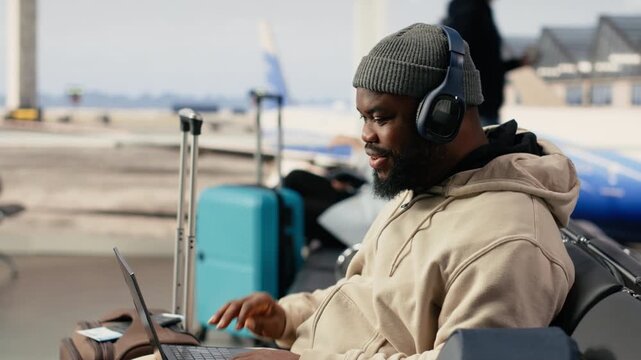 African american man on video conference call using airport internet, speaking to colleagues during online meeting while seated in the terminal waiting area. Digital communication and mobility.
