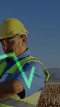 Vertical video: Wind tech checking watch after neon graph passing over chest, tracking wind turbine